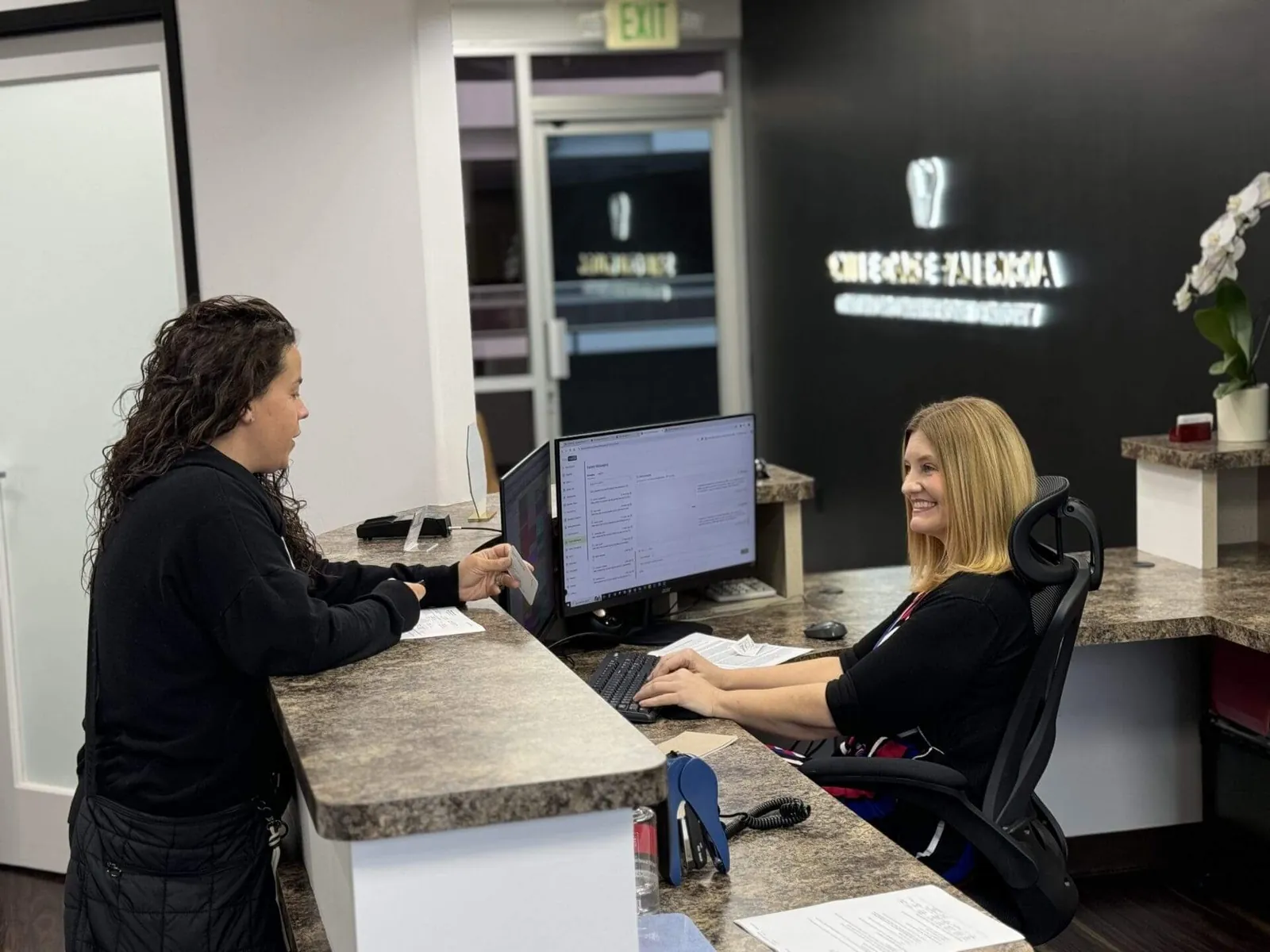 Two women at a dental office reception desk.